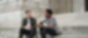 Two men sitting on the steps of an old building and chatting with a coffee