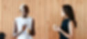 Two women standing up and chatting while having a coffee